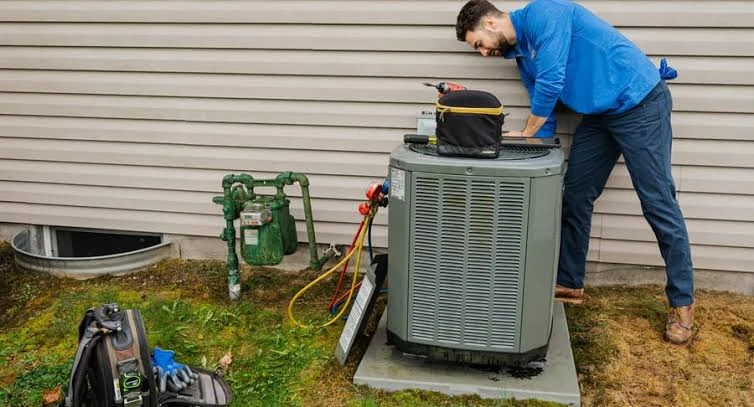 Technician maintaining an outdoor AC condenser beside a home